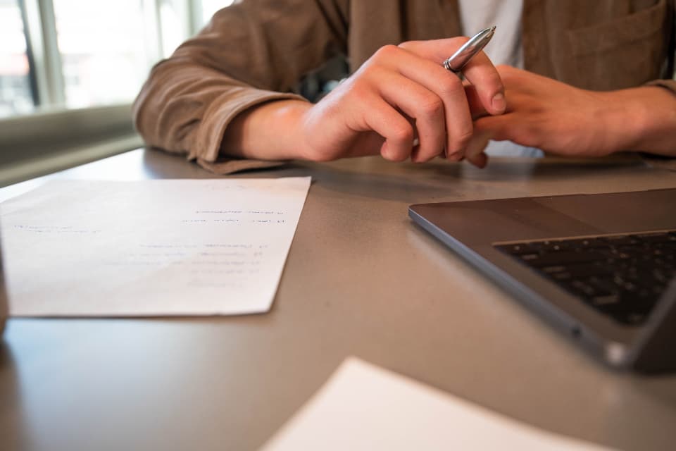 Someone making notes beside a laptop while planning their money